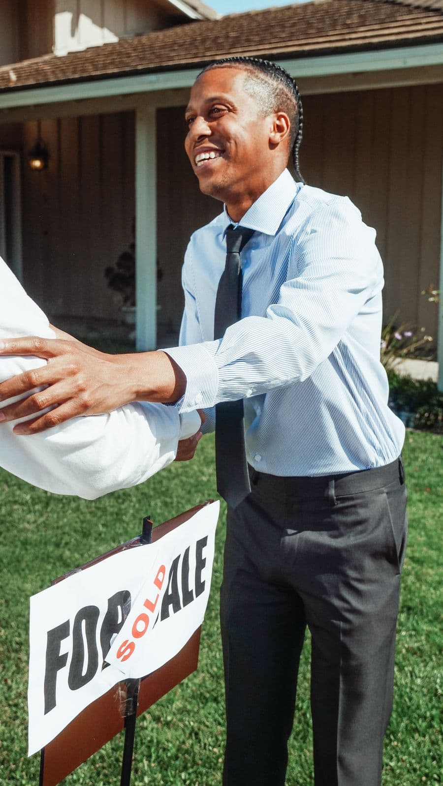 Estate agent shaking hands beside a sold sign