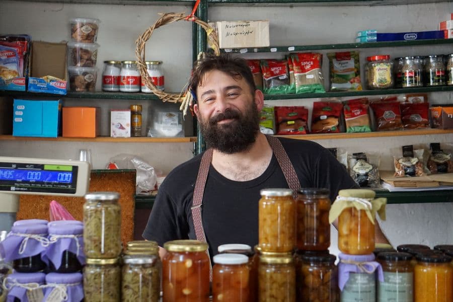 Shopkeeper behind shelves of jars in a small deli